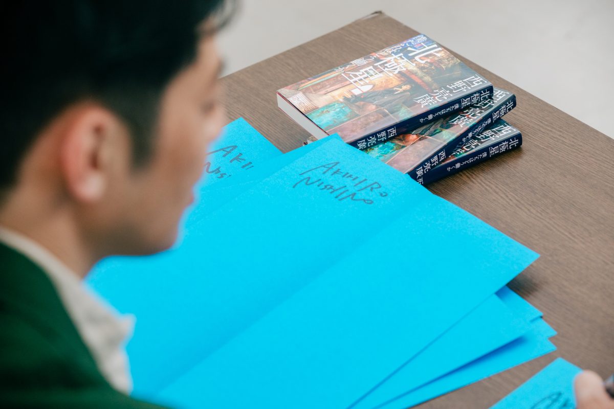 新刊『北極星　僕たちはどう働くか』に次々とサインをしていく西野氏。